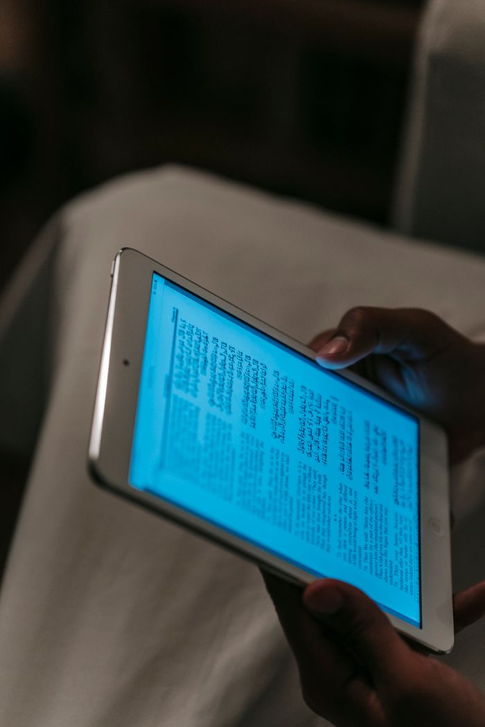 From above of crop unrecognizable person in white clothes browsing tablet in dark room